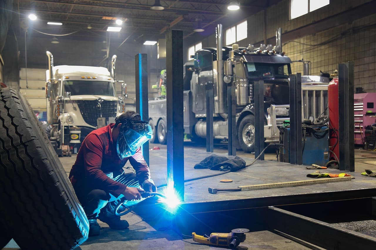 A mechanic welding under bright lights in a workshop with vehicle lifts